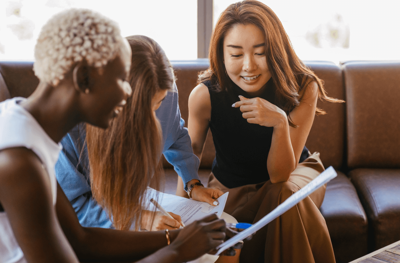 Three business women on a couch looking at paper work and smiling